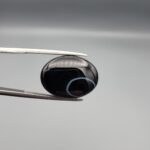 "Natural Black Sulemani Aqeeq Agate oval cabochon gemstone 15.30 carat with white eye ring pattern held in tweezers"