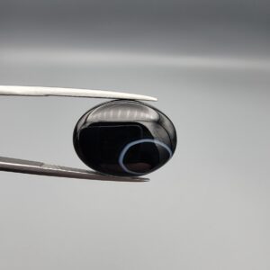 "Natural Black Sulemani Aqeeq Agate oval cabochon gemstone 15.30 carat with white eye ring pattern held in tweezers"