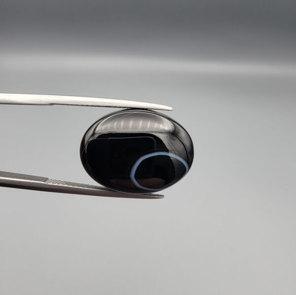 "Natural Black Sulemani Aqeeq Agate oval cabochon gemstone 15.30 carat with white eye ring pattern held in tweezers"
