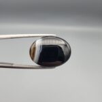 "Natural Black Banded Sulemani Aqeeq Agate oval cabochon gemstone 14.00 carat with white side banding held in tweezers"