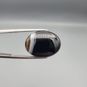 "Natural Black Banded Sulemani Aqeeq Agate oval cabochon gemstone 14.00 carat with white side banding held in tweezers"