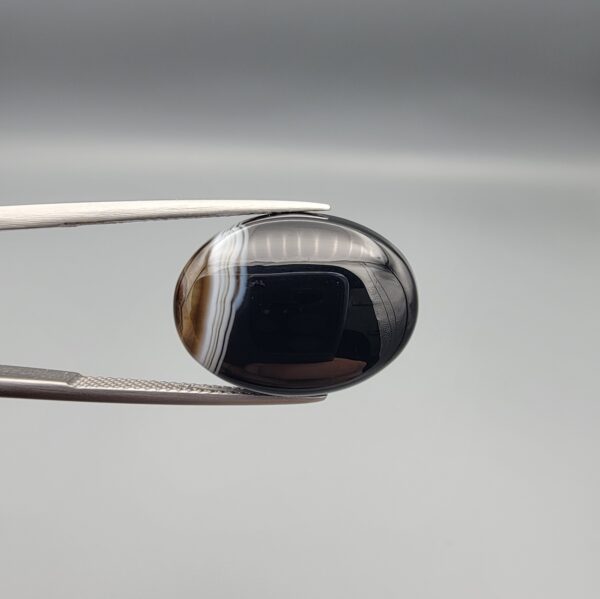 "Natural Black Banded Sulemani Aqeeq Agate oval cabochon gemstone 14.00 carat with white side banding held in tweezers"