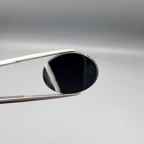"Natural Black Banded Sulemani Aqeeq Agate oval cabochon gemstone 14.00 carat with white side banding held in tweezers"
