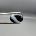 "Natural Black Banded Sulemani Aqeeq Agate oval cabochon gemstone 14.27 carat with curved white and brown band held in tweezers"
