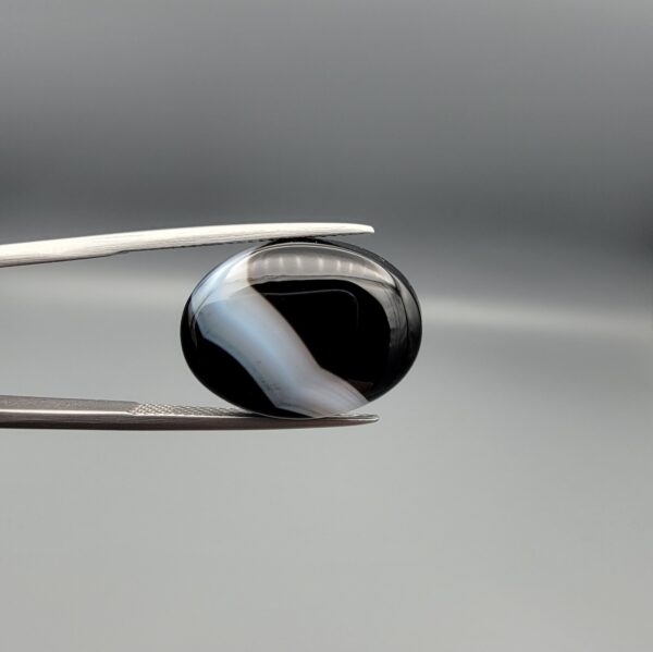 "Natural Black Banded Sulemani Aqeeq Agate oval cabochon gemstone 14.27 carat with curved white and brown band held in tweezers"