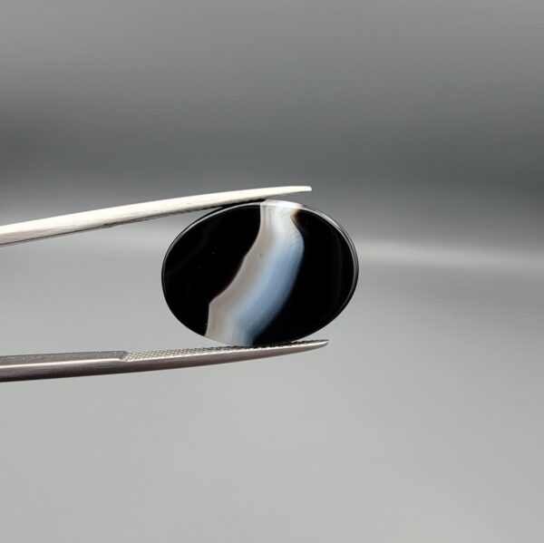 "Natural Black Banded Sulemani Aqeeq Agate oval cabochon gemstone 14.27 carat with curved white and brown band held in tweezers"