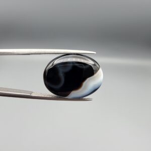 "Natural Black Banded Sulemani Aqeeq Agate oval cabochon gemstone 14.03 carat with horizontal white and brown wave band held in tweezers"