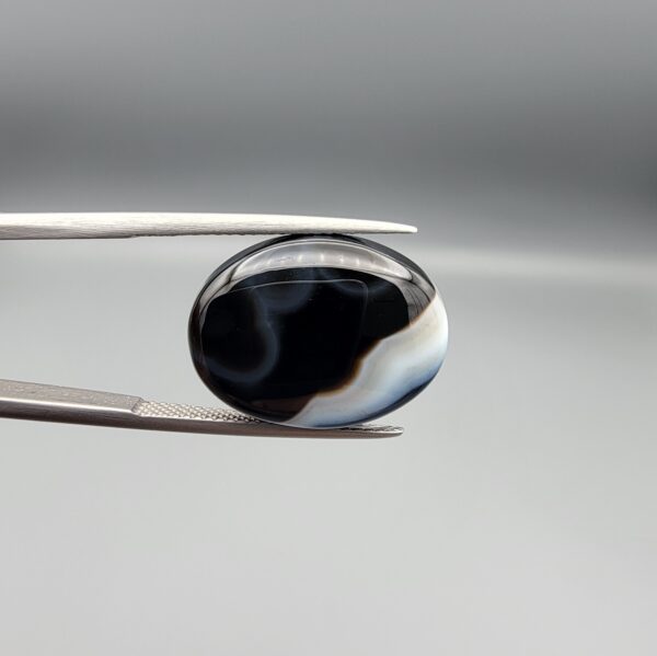 "Natural Black Banded Sulemani Aqeeq Agate oval cabochon gemstone 14.03 carat with horizontal white and brown wave band held in tweezers"