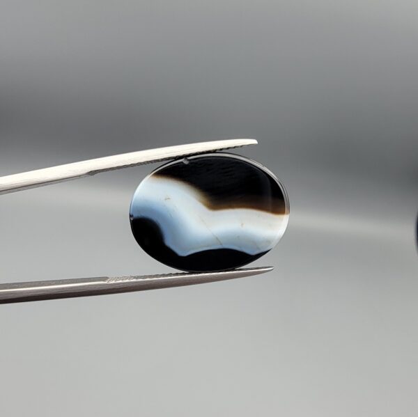 "Natural Black Banded Sulemani Aqeeq Agate oval cabochon gemstone 14.03 carat with horizontal white and brown wave band held in tweezers"