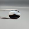 "Natural Black Banded Sulemani Aqeeq Agate oval cabochon gemstone 15.53 carat with scalloped white and brown cloud pattern held in tweezers"