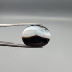 "Natural Black Banded Sulemani Aqeeq Agate oval cabochon gemstone 15.53 carat with scalloped white and brown cloud pattern held in tweezers"