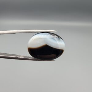 "Natural Black Banded Sulemani Aqeeq Agate oval cabochon gemstone 15.53 carat with scalloped white and brown cloud pattern held in tweezers"