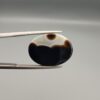 "Natural Black Banded Sulemani Aqeeq Agate oval cabochon gemstone 15.53 carat with scalloped white and brown cloud pattern held in tweezers"
