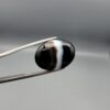 "Natural Black Banded Sulemani Aqeeq Agate oval cabochon gemstone 15.08 carat with vertical white and brown side band held in tweezers"