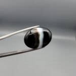 "Natural Black Banded Sulemani Aqeeq Agate oval cabochon gemstone 15.08 carat with vertical white and brown side band held in tweezers"