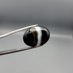 "Natural Black Banded Sulemani Aqeeq Agate oval cabochon gemstone 15.08 carat with vertical white and brown side band held in tweezers"