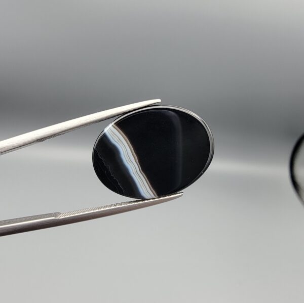 "Natural Black Banded Sulemani Aqeeq Agate oval cabochon gemstone 15.08 carat with vertical white and brown side band held in tweezers"