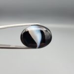 "Natural Black Banded Sulemani Aqeeq Agate oval cabochon gemstone 15.15 carat with diagonal white and brown swirl band held in tweezers"
