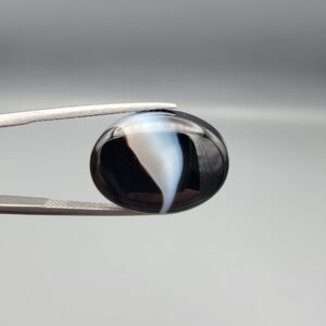 "Natural Black Banded Sulemani Aqeeq Agate oval cabochon gemstone 15.15 carat with diagonal white and brown swirl band held in tweezers"