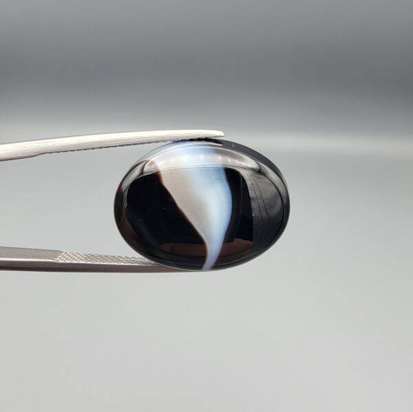 "Natural Black Banded Sulemani Aqeeq Agate oval cabochon gemstone 15.15 carat with diagonal white and brown swirl band held in tweezers"