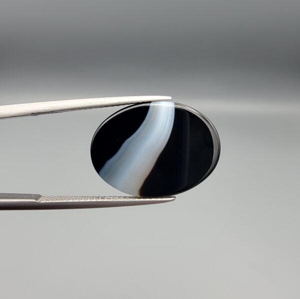 "Natural Black Banded Sulemani Aqeeq Agate oval cabochon gemstone 15.15 carat with diagonal white and brown swirl band held in tweezers"