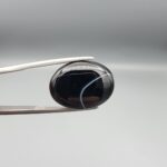 "Natural Black Banded Sulemani Aqeeq Agate oval cabochon gemstone 15.33 carat with thin white thread line held in tweezers"