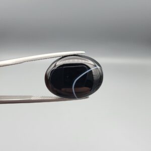 "Natural Black Banded Sulemani Aqeeq Agate oval cabochon gemstone 15.33 carat with thin white thread line held in tweezers"