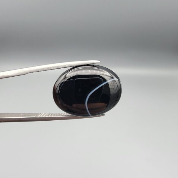 "Natural Black Banded Sulemani Aqeeq Agate oval cabochon gemstone 15.33 carat with thin white thread line held in tweezers"