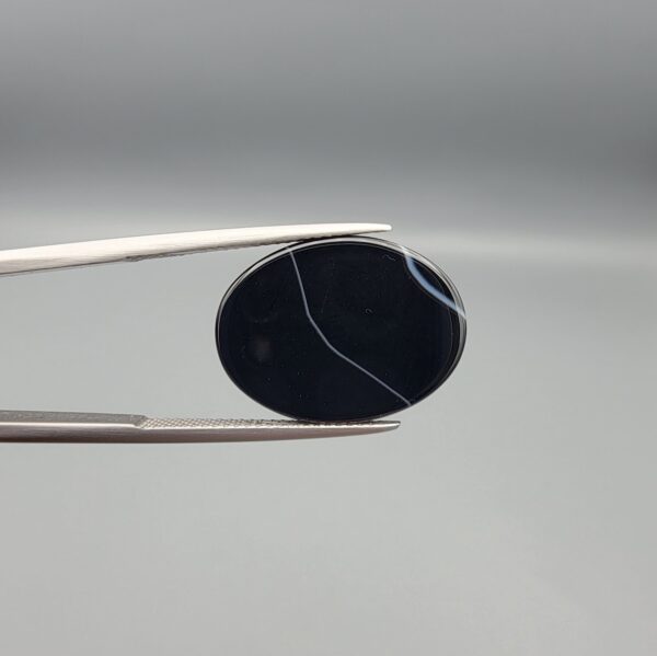 "Natural Black Banded Sulemani Aqeeq Agate oval cabochon gemstone 15.33 carat with thin white thread line held in tweezers"