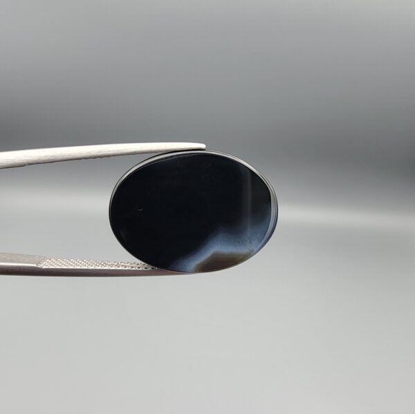 "Natural Black Banded Sulemani Aqeeq Agate oval cabochon gemstone 14.25 carat, plain black front with wide white and grey band on reverse, held in tweezers"