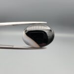 "Natural Black Banded Sulemani Aqeeq Agate oval cabochon gemstone 14.14 carat with diagonal white and brown corner band held in tweezers"