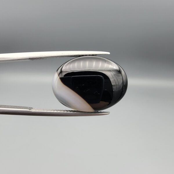 "Natural Black Banded Sulemani Aqeeq Agate oval cabochon gemstone 14.14 carat with diagonal white and brown corner band held in tweezers"