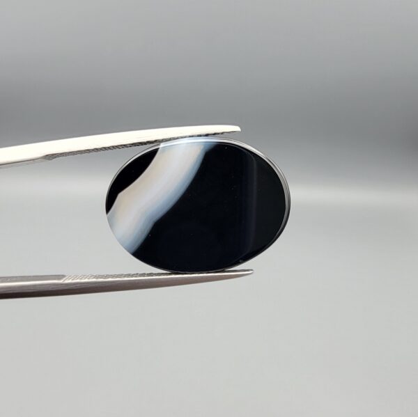 "Natural Black Banded Sulemani Aqeeq Agate oval cabochon gemstone 14.14 carat with diagonal white and brown corner band held in tweezers"