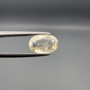 "Natural unheated Yellow Sapphire Pukhraj gemstone 2.47 carat oval cut from Sri Lanka Ceylon held in tweezers showing pale golden color and natural inclusions"