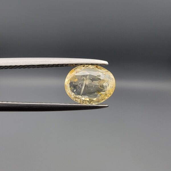"Natural unheated Yellow Sapphire Pukhraj gemstone 2.05 carat oval cut from Sri Lanka Ceylon held in tweezers showing visible natural crystal inclusion"