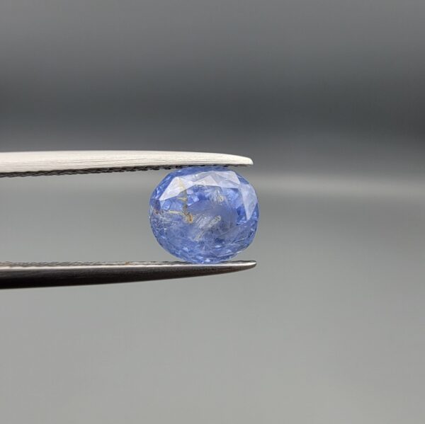 "Natural unheated Blue Sapphire Neelam gemstone 3.02 carat oval cut from Sri Lanka Ceylon held in tweezers showing cornflower blue color and natural inclusions"