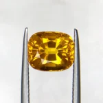 High-resolution photograph of an official Galaxy Gemological Institute (GGI) Gemstone Report certificate (No. KHI2609940326) dated 14 September 2026 for a 4.45-carat transparent Orangish Yellow natural cushion mixed-cut Yellow Sapphire from Madagascar.
