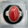 ​A premium men's luxury ring crafted from high-polish sterling silver, showcasing a massive 18.10-carat natural Japanese Red Coral (Marjan) cabochon as the central focal point. The vibrant red oval coral is securely held by a decorative multi-prong crown bezel setting on a thick, durable silver band, beautifully presented inside a professional display cushion case.