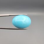 "Natural Razaki Feroza Turquoise gemstone 20.67 carat oval cabochon from Iran, front smooth sky-blue face and back natural matrix view, held in tweezers"
