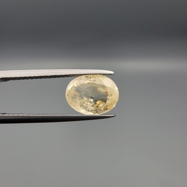 "Natural unheated Yellow Sapphire Pukhraj gemstone 2.88 carat oval cut from Sri Lanka Ceylon held in tweezers showing pale golden color and natural feather inclusions"
