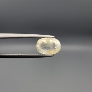 Natural unheated Yellow Sapphire Pukhraj gemstone 2.25 carat oval cut from Sri Lanka Ceylon held in tweezers showing pale ivory tone and natural inclusions