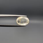 "Natural unheated Yellow Sapphire Pukhraj gemstone 2.15 carat oval cut from Sri Lanka Ceylon held in tweezers showing pale color and visible natural needle inclusion"