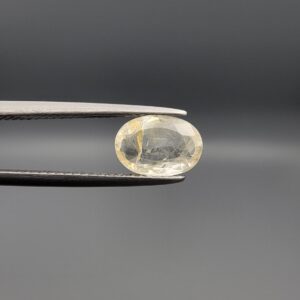 "Natural unheated Yellow Sapphire Pukhraj gemstone 2.15 carat oval cut from Sri Lanka Ceylon held in tweezers showing pale color and visible natural needle inclusion"
