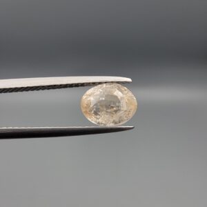 "Natural unheated Yellow Sapphire Pukhraj gemstone 2.58 carat oval cut from Sri Lanka Ceylon held in tweezers showing peachy-cream tone and natural inclusions"