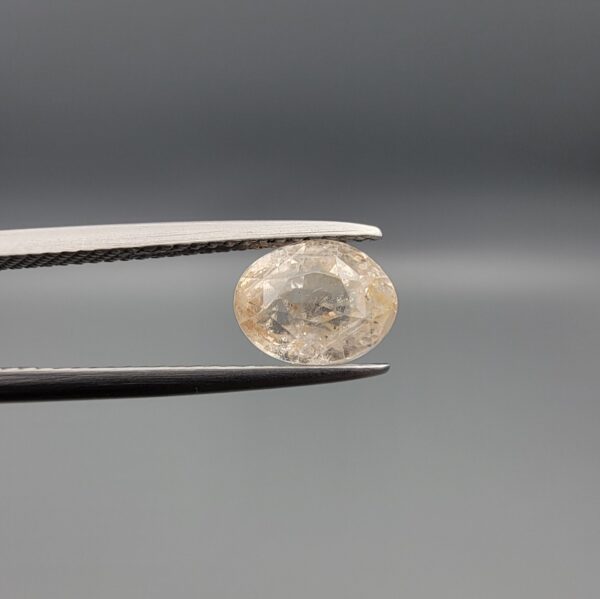 "Natural unheated Yellow Sapphire Pukhraj gemstone 2.58 carat oval cut from Sri Lanka Ceylon held in tweezers showing peachy-cream tone and natural inclusions"