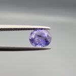 "Natural unheated Purple Sapphire Khooni Neelam gemstone 1.38 carat oval cut from Sri Lanka Ceylon held in tweezers showing vivid violet color and natural rust inclusions"