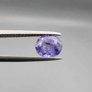 "Natural unheated Purple Sapphire Khooni Neelam gemstone 1.38 carat oval cut from Sri Lanka Ceylon held in tweezers showing vivid violet color and natural rust inclusions"