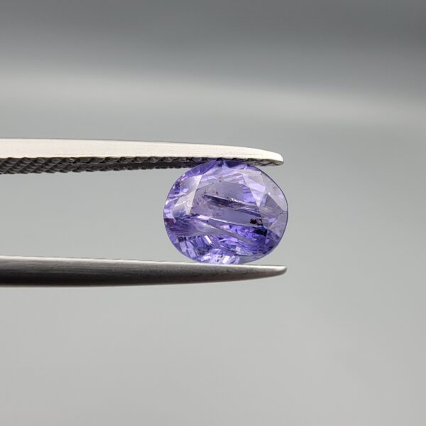 "Natural unheated Purple Sapphire Khooni Neelam gemstone 1.38 carat oval cut from Sri Lanka Ceylon held in tweezers showing vivid violet color and natural rust inclusions"