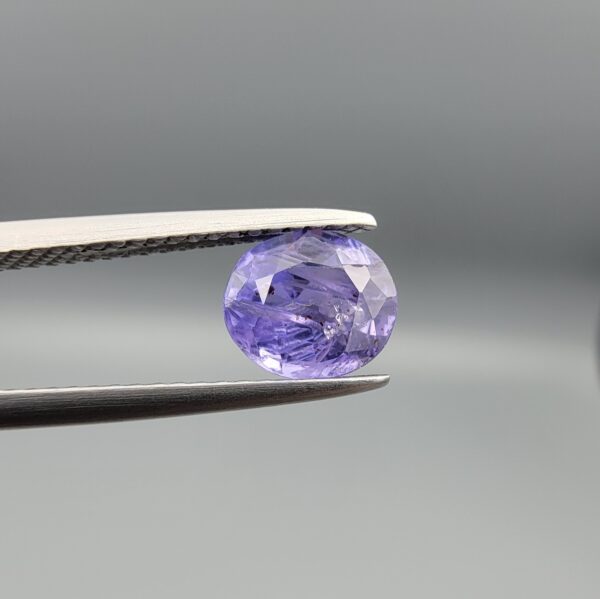 "Natural unheated Purple Sapphire Khooni Neelam gemstone 1.38 carat oval cut from Sri Lanka Ceylon held in tweezers showing vivid violet color and natural rust inclusions"