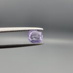 ​A premium, beautifully faceted 0.69-carat natural Purple Sapphire gemstone is held securely in metal tweezers against a clean, neutral grey background. The loose cushion-cut corundum gem displays a soft lavender-purple hue, serving as an indisputable signature of its rare unheated, earth-mined origin.